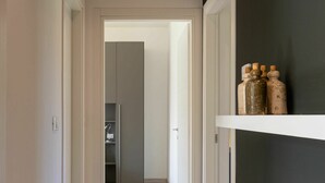 Un couloir au plancher de bois mène à une pièce où se trouve une armoire grise et une étagère remplie de bouteilles.