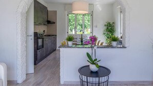 Une cuisine moderne dotée d’un îlot central, un coin repas avec une table ronde, et une vue sur une salle à manger accessible par une arche.