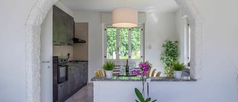 A modern kitchen with a central island, a dining area with a round table, and a view through an archway to a dining room.