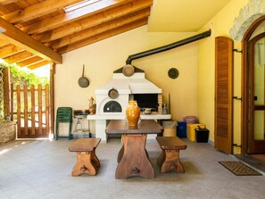 Una cuina rústica a l'aire lliure amb un forn de llenya, dos tamborets de fusta i una taula.