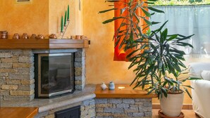 A cozy living room with a stone fireplace, a large potted plant, and a view of greenery outside. - Beautiful apartment for 5 people with hot tub, WIFI, TV, terrace and pets allowed (Colico)