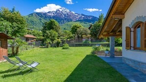 A house with a garden, a mountain in the background, and a clear sky. - Beautiful apartment for 5 people with hot tub, WIFI, TV, terrace and pets allowed (Colico)