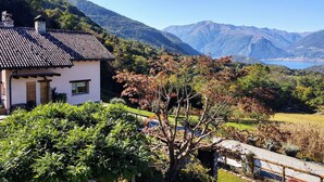Une maison avec un toit en tuiles, entourée d’une végétation luxuriante et avec des montagnes en arrière-plan.