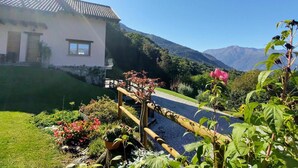 Une maison avec un toit en tuiles, un petit balcon et un jardin où poussent différentes plantes et fleurs.