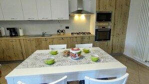Une cuisine compacte avec des meubles blancs, une cuisinière à gaz et un four à micro-ondes. On y trouve une table à manger avec des chaises et une nappe à motifs.