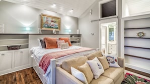 A bedroom with a bed, a sofa, a painting, a mirror, and built-in shelving. - Sea View Carriage House - Close to Beach/Coquina Pool/Main Street! Free Bikes, Fitness & Tennis! (Rosemary Beach)