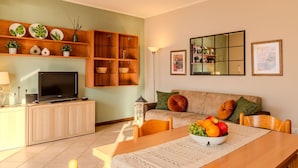 A modern living room with a TV, wooden cabinets, a sofa, and a dining table with fruit.