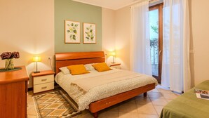 A bedroom with a wooden bed, two bedside lamps, a nightstand, a green rug, and two framed botanical prints on the wall.