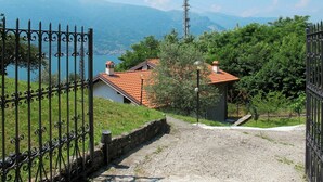 A gravel path leading to a house with a red-tiled roof, surrounded by greenery and overlooking a lake with mountains in the background. - Beautiful private villa for 7 guests with WIFI, TV, terrace and pets allowed (Vestreno)