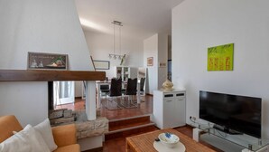 Una sala de estar moderna con un sofá, una mesa de centro, un televisor y un comedor al fondo.
