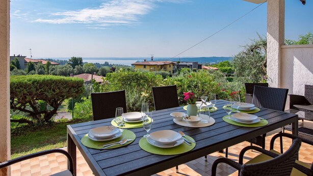 Mesa de comedor al aire libre con vista a un lago y edificios a lo lejos.