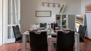 Un comedor con una mesa blanca dispuesta para cuatro, sillas negras, un armario blanco con libros y un espejo en la pared.