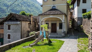Un bâtiment traditionnel doté d’un clocher, d’une petite aire de jeux et d’un sentier en pierre menant à un paysage montagneux.