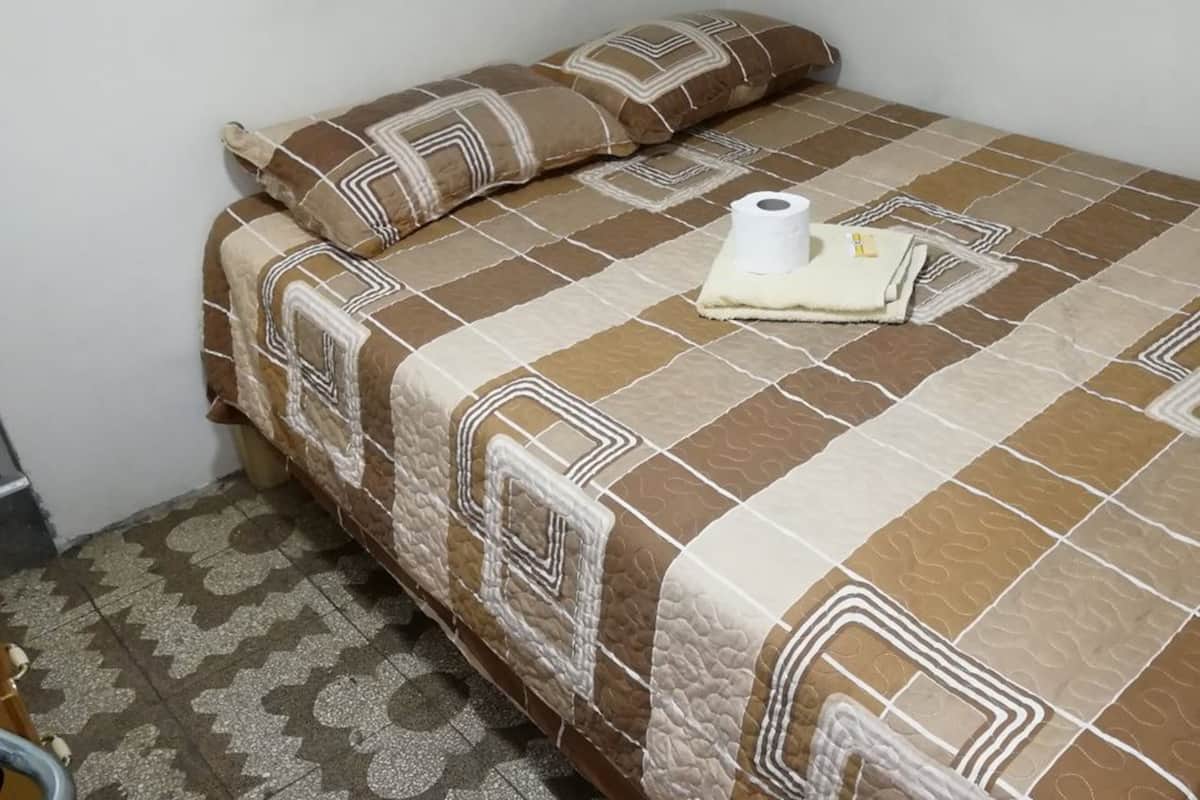 A bed with a patterned bedspread and pillows, a roll of toilet paper, and a folded towel on the bed.