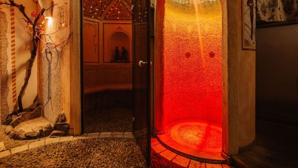 Un intérieur avec un mur en pierre, une porte en bois et une zone circulaire éclairée en rouge.