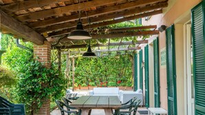 Un patio al aire libre con una pérgola de madera, una mesa con sillas y vistas a un jardín exuberante.