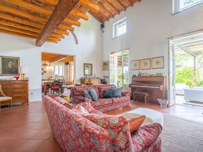 Uma sala de estar espaçosa com um sofá grande, um piano e um espaço para refeições.