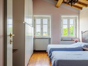 Habitació petita i ben il·luminada amb dos llits, un radiador i una finestra amb vista a vegetació.