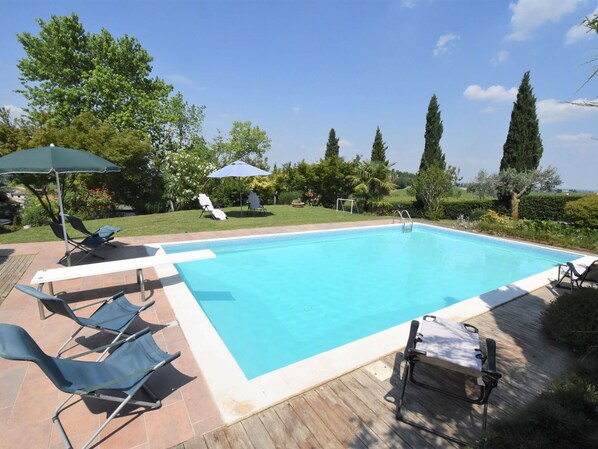 Una piscina rectangular amb una terrassa de fusta i gandules.