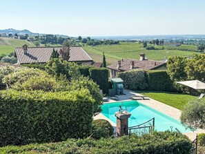 A residential property with a swimming pool, surrounded by well-maintained hedges and a view of vineyards.