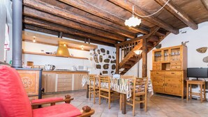 Ein gemütlicher Wohnbereich mit Holzbalkendecke, einem Esstisch mit Stühlen, einem roten Sofa und einer Küche im Hintergrund.