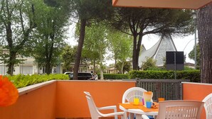 A balcony with orange walls, white chairs, and a table with drinks. - Nice apartment for 5 guests with WIFI, A/C, TV, terrace and pets allowed (San Michele Al Tagliamento)