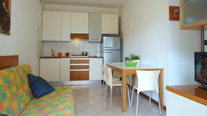 A compact living space with a kitchenette, a dining area, and a sofa with a colorful blanket. - Nice apartment for 5 guests with WIFI, A/C, TV, terrace and pets allowed (San Michele Al Tagliamento)