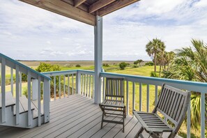 A wooden deck with a railing, two wooden benches, and a view of a grassy field with palm trees.