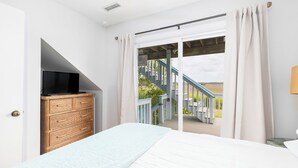 A bedroom with a bed, a television on a dresser, and a view of a wooden deck and stairs.
