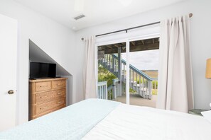 A bedroom with a bed, a television on a dresser, and a view of a wooden deck and stairs.