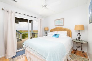 A bedroom with a bed, two bedside lamps, a framed artwork, and a view of the outdoors.