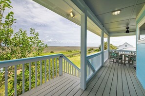 A covered porch with a view of a grassy field and a house in the background. - Once Upon A Tide ~ Dog Friendly! ~ Ocean + Marsh Views (Folly Beach)