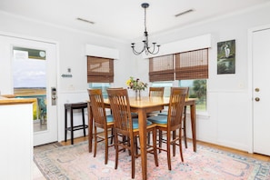 A dining area with a wooden table, chairs, a chandelier, and a view through the windows.
