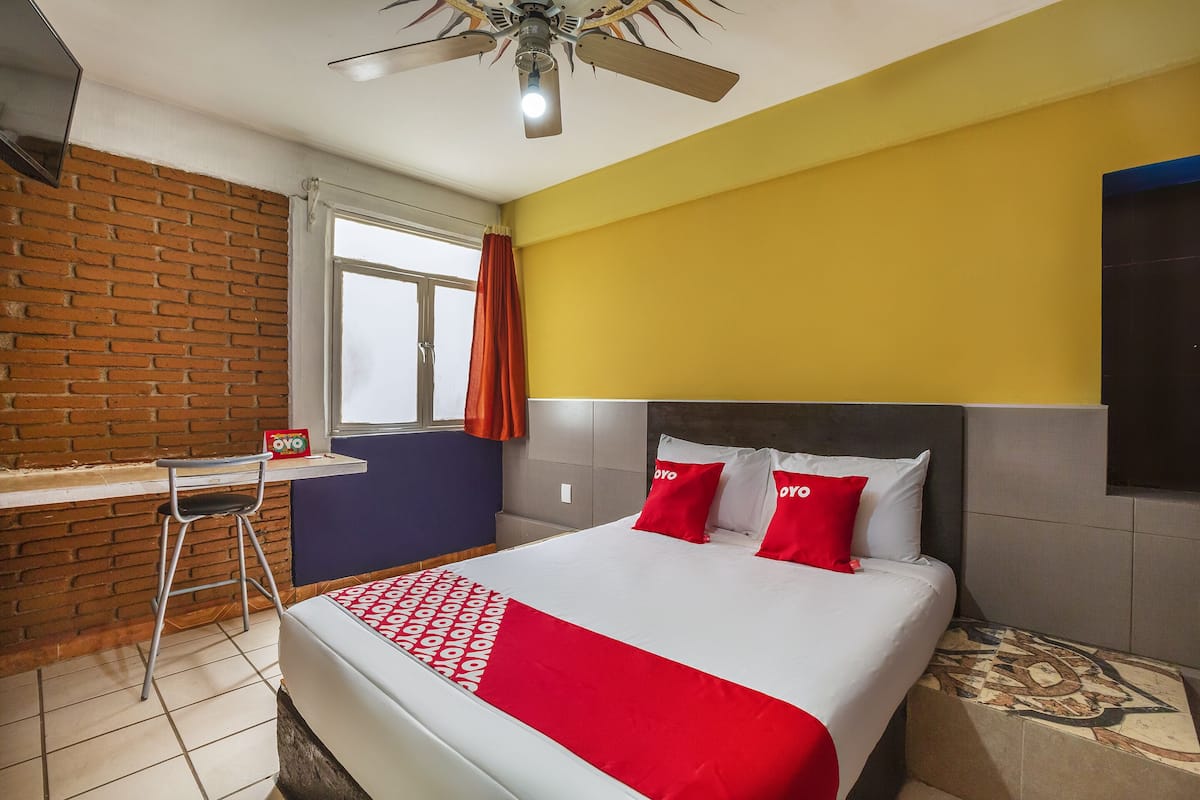 A hotel room with a bed, a desk, and a window.