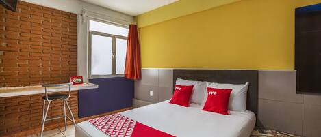 A hotel room with a bed, a desk, and a window.