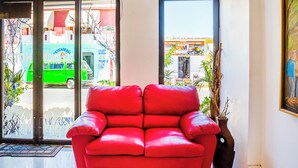 A red leather sofa in a room with a large window, a potted plant, and a door leading outside.
