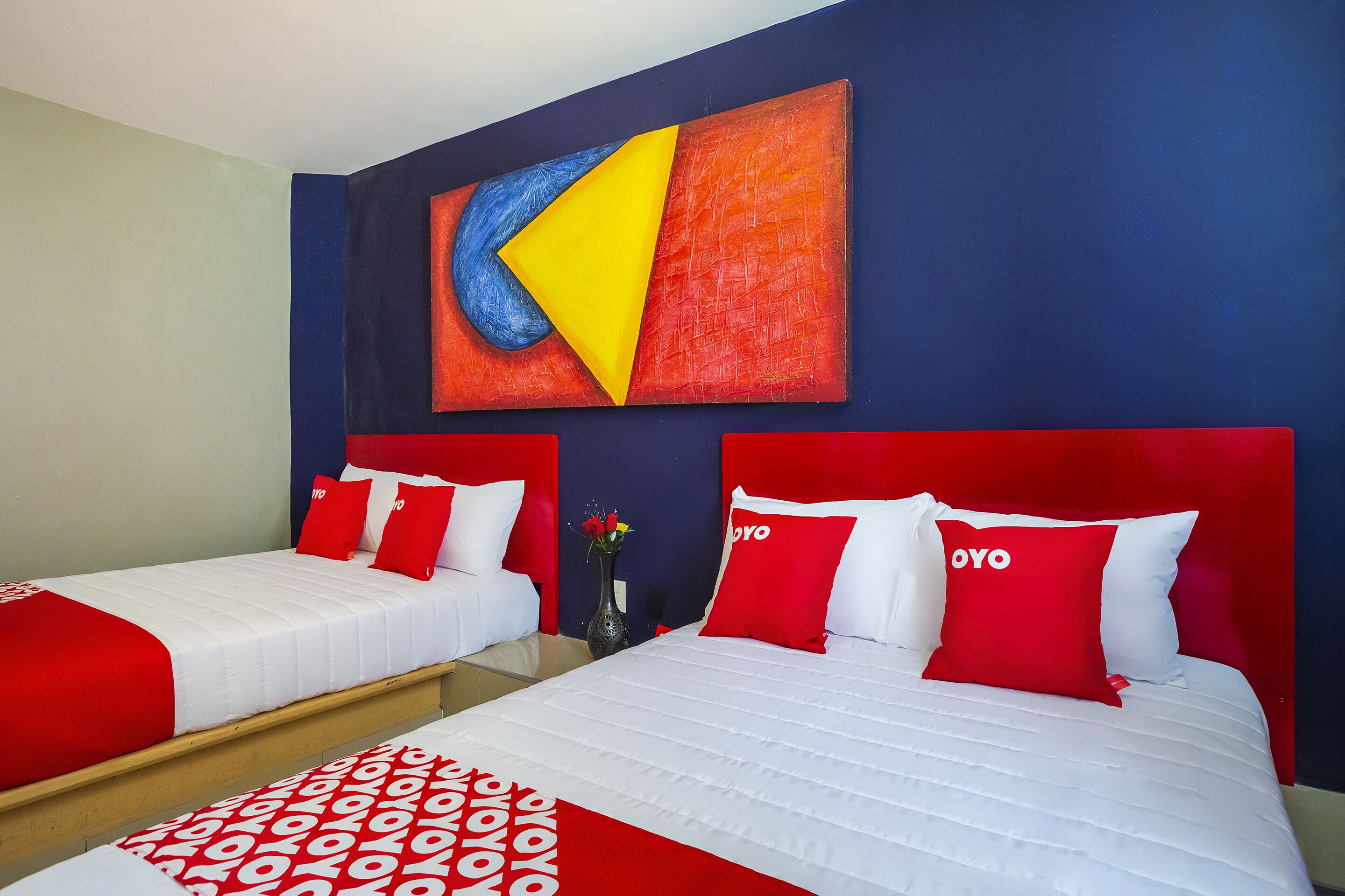 A hotel room with two beds, each with red and white bedding, and a large abstract painting on the wall.