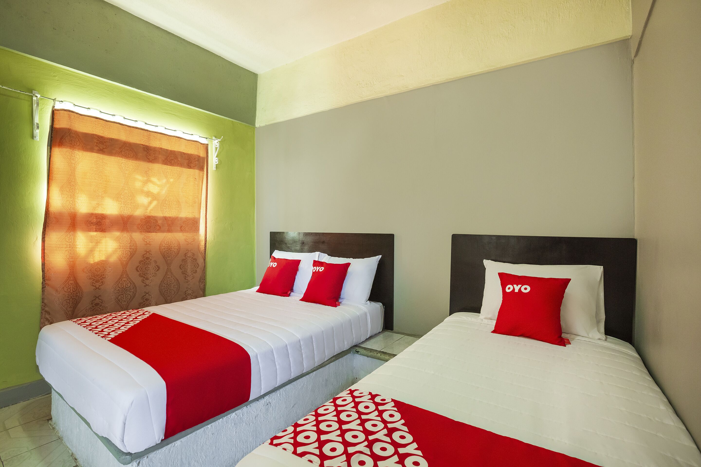 Quarto de hotel com duas camas, cada uma com colcha vermelha e branca e almofadas combinando.