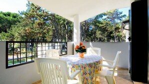 Een balkon met een tafel en stoelen, een bloempot en uitzicht op bomen.