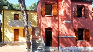 A two-story building with a red facade, a staircase leading to the upper floor, and a patio area with outdoor seating. - Lovely apartment for 7 people with A/C, WIFI, TV and pets allowed (Rosolina)