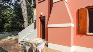 A building with a red exterior, a staircase leading to an entrance, and a patio area with a table and chairs. - Lovely apartment for 7 people with A/C, WIFI, TV and pets allowed (Rosolina)