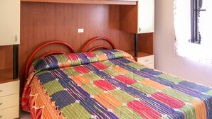 A bed with a colorful quilt, wooden headboard, and red metal headboard supports. - Lovely apartment for 7 people with A/C, WIFI, TV and pets allowed (Rosolina)