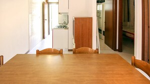 A dining area with a wooden table and chairs, a kitchen in the background, and a shower room visible through an open door. - Lovely apartment for 7 people with A/C, WIFI, TV and pets allowed (Rosolina)