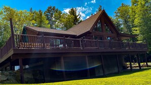 A wooden cabin with a balcony, surrounded by a grassy lawn and trees.