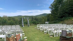 An outdoor wedding venue with rows of white chairs and a wooden aisle.
