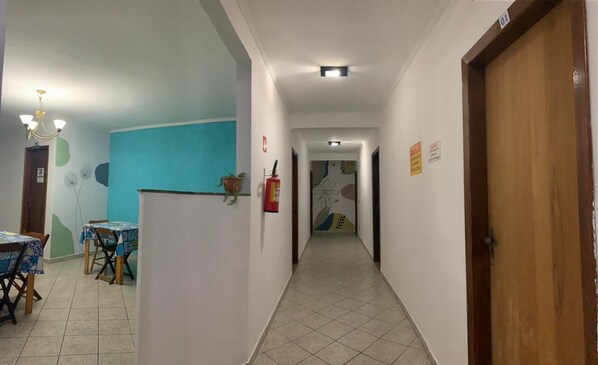 A hallway with a dining area on the left, a fire extinguisher on the wall, and a door on the right. - Pousada Martin de Sá (Caraguatatuba)