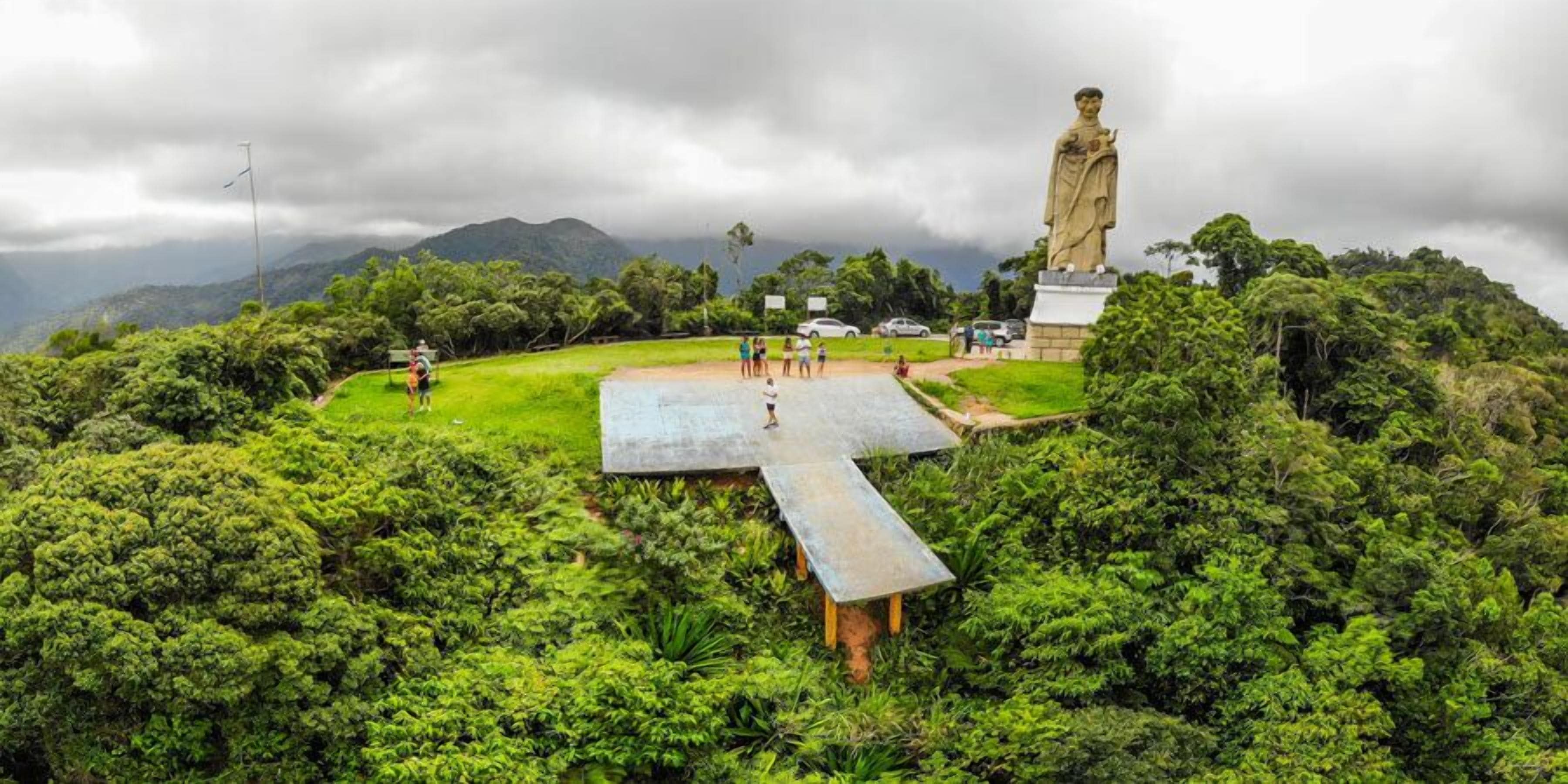 A statue in a lush green park with a large cross-shaped platform in the foreground.