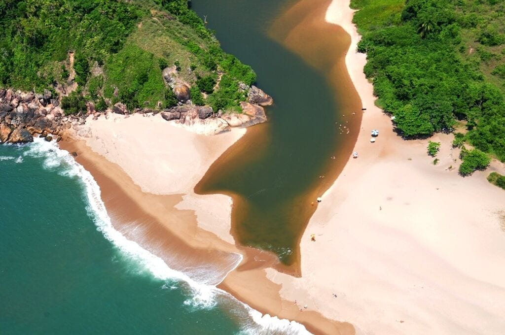An aerial view of a beach with clear waters, sandy shores, and lush greenery.