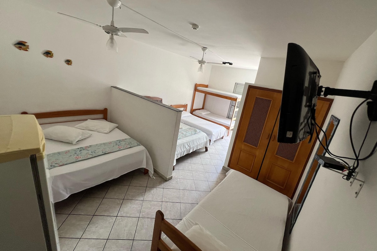 Quarto de hotel com duas camas de solteiro, um guarda-roupa de madeira, uma televisão e ventoinhas de teto.