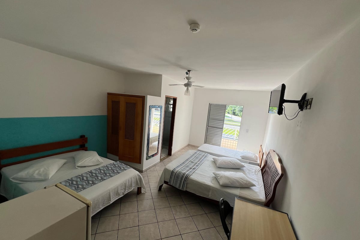 Quarto com duas camas, guarda-roupa, escrivaninha e ventoinha no teto.